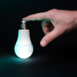 A hand gently touching a glowing LED bulb, symbolizing new ideas and innovation.