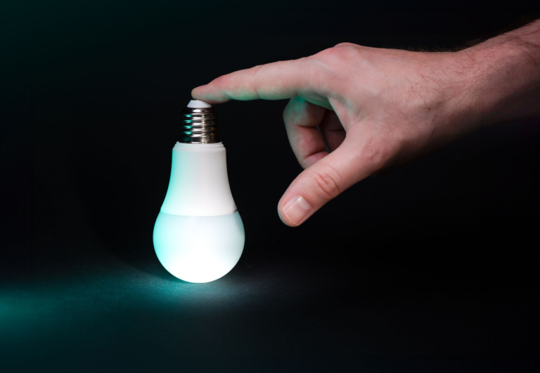 A hand gently touching a glowing LED bulb, symbolizing new ideas and innovation.
