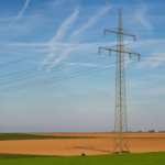High voltage power line standing tall in a vast agricultural field under a clear blue sky in Germany.