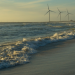 Peaceful beach scene with ocean waves and wind turbines at sunset, showcasing renewable energy.