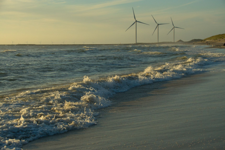 Peaceful beach scene with ocean waves and wind turbines at sunset, showcasing renewable energy.