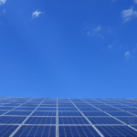 A low angle view of solar panels under a bright blue sky with clouds.