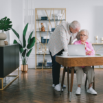 Senior couple using a laptop while discussing something in their modern living room.
