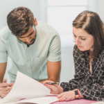 Real estate agent assisting first-time homebuyer with documents inside a bright room.