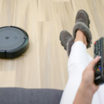 A person relaxing on a couch with a robotic vacuum cleaning the hardwood floor.