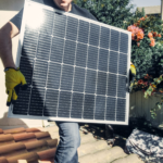 Technician carrying solar panel on rooftop. Clean energy installation outdoors.