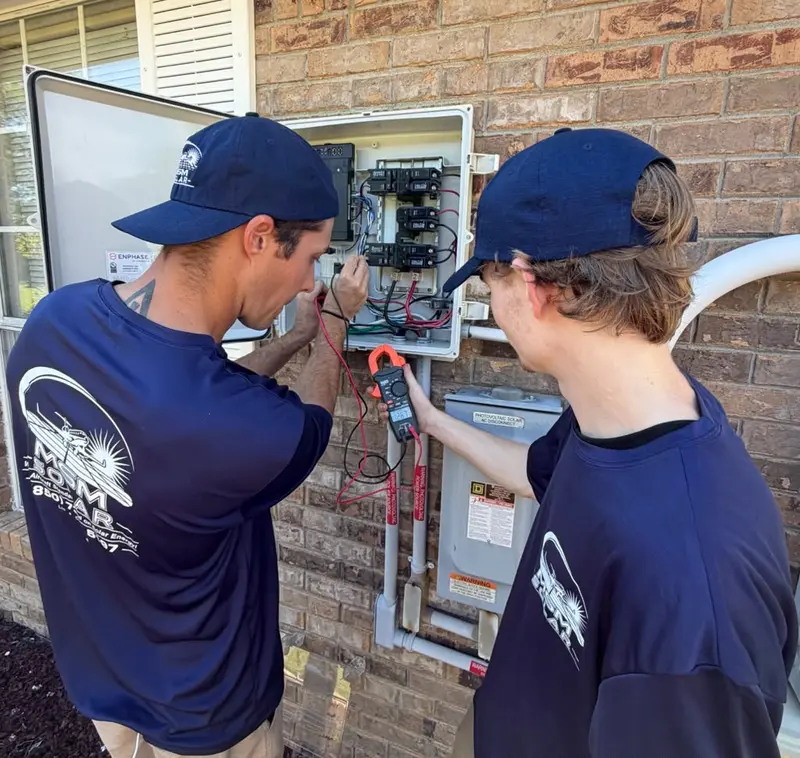 Two MSM Solar technicians testing a homeowner's solar combiner box with a clamp meter