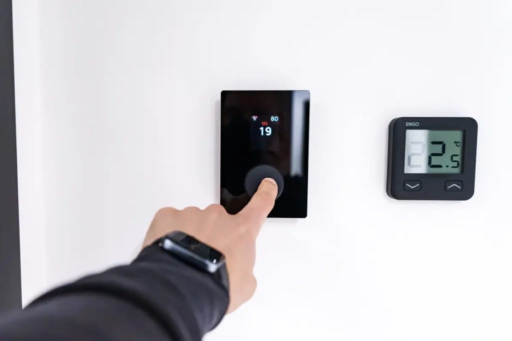 Hand adjusting a digital thermostat on a wall at home